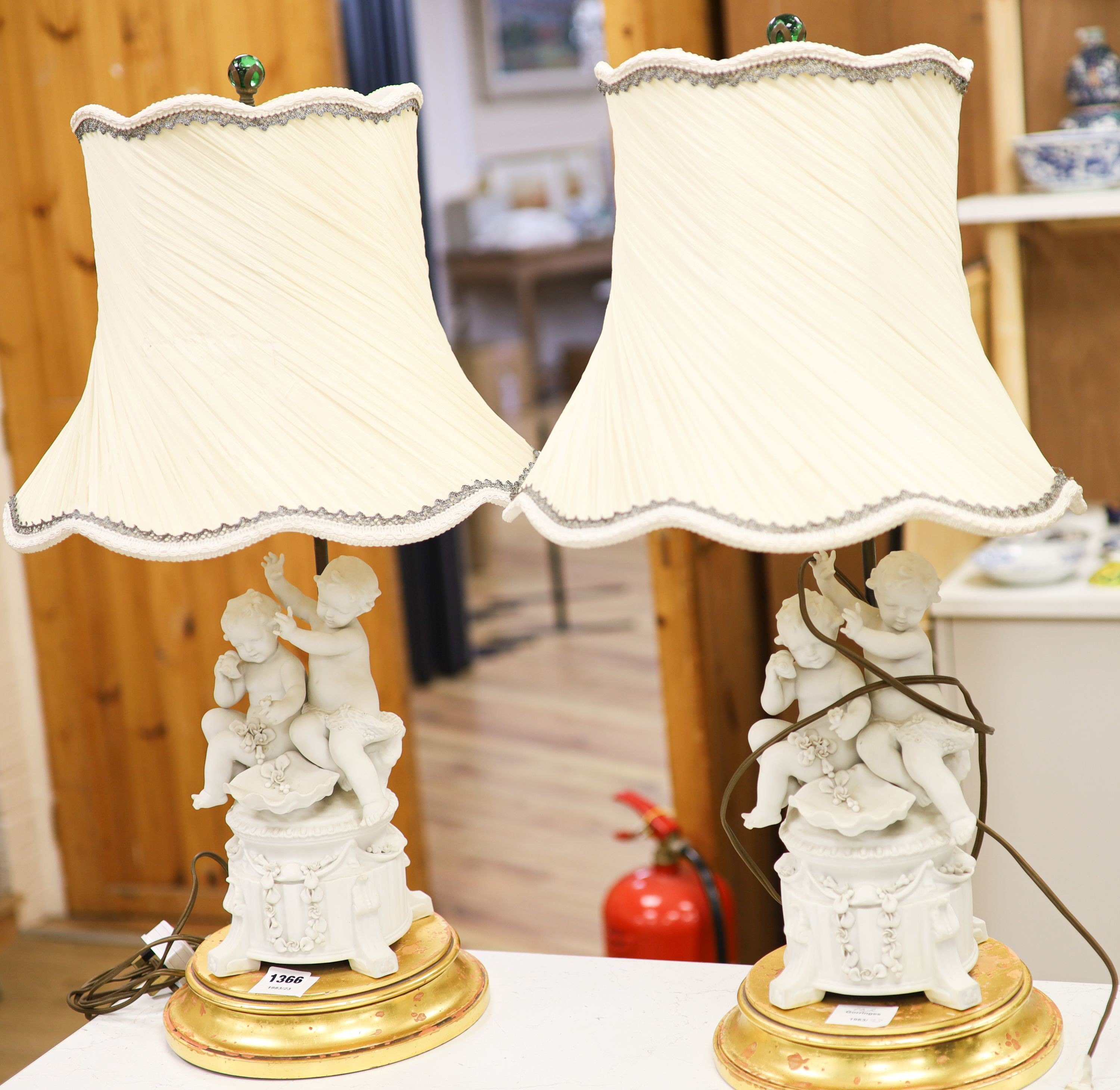 A pair of Sevres style biscuit porcelain groups of putti, fitted as a table lamps with shades 69cm total height incl shades